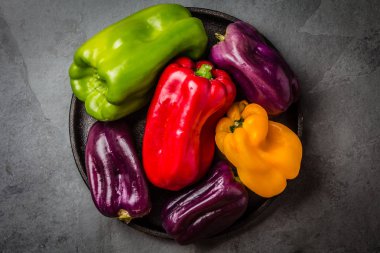 Birçok renkli biber ppurple, kırmızı, yeşil, sarı siyah plaka tablo, gri kayrak arka plan üzerinde