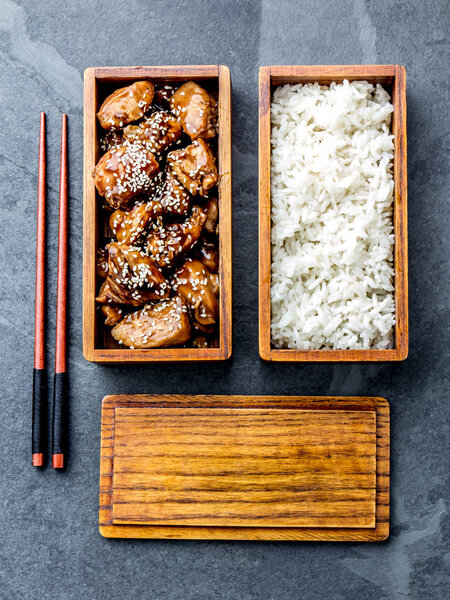 Японская еда. Куриные терияки с рисом в деревянной коробке для обедов. фон с шифер, вид сверху
