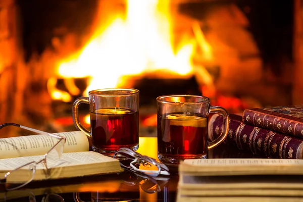Sıcak bir içecek veya alkollü içki veya kırmızı şarap mulled ve antika kitap sıcak şömine önünde iki cam kupaları. Büyülü rahat rahat bir atmosfer ateş yakın. Sonbahar ya da kış konsepti