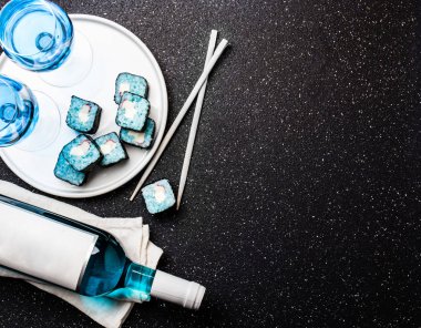 Mavi suşi rulo ve siyah arka plan üzerine mavi şarap chardonnay. İspanyolca mavi şarap, trendy içki, süslü şarap, üstten görünüm. Kopya alanı.