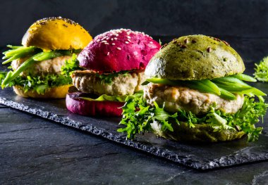 Colored green, yellow and purple burgers on slate board. Close up clipart