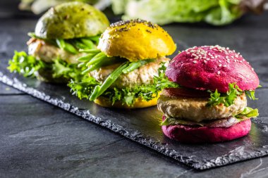 Colored green, yellow and purple burgers on slate board. Close up clipart