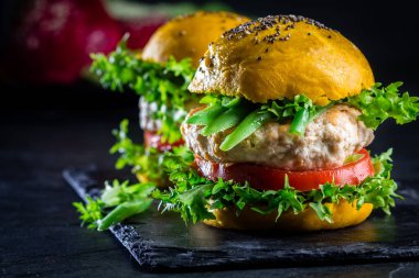 Colored yellow burgers. Homemade American chicken burgers hamburgers with turmeric curcuma and chia buns and vegetables. Trendy food. Close up, slate background. clipart