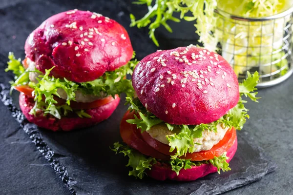 Colored purple beetroot burgers. Chicken burgers hamburgers with beetroot pink buns and vegetables