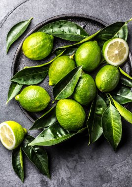 Yeşil limon kireç ile taze siyah plaka, arduvaz arka plan üzerinde bırakır. Üstten görünüm