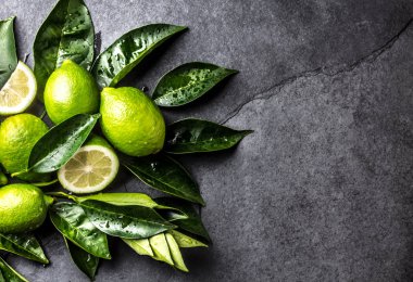 Yeşil limon kireç ile taze siyah arduvaz arka plan üzerine bırakır. Üstten görünüm