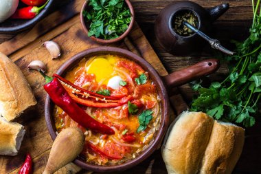 Chilean food. Picante caliente. Tomatoes, onion, chili fried with eggs in clay pan, wooden background clipart