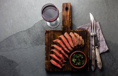 Sığır eti Orta az pişmiş biftek ahşap tahta, arduvaz arka plan üzerinde kırmızı şarap üzerinde dilim