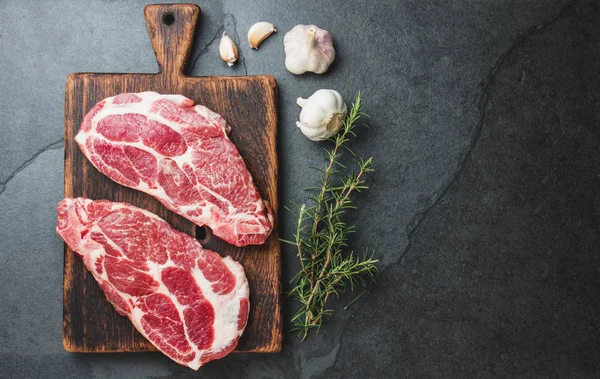 Filetes de cerdo crudos con condimento sobre tabla de madera. Fondo de pizarra gris — Foto de Stock