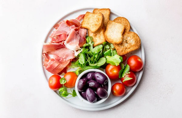 Antipasto Plate with dried bread, ham serrano, tomato cherry and purple olives. White background. — Stock Photo, Image