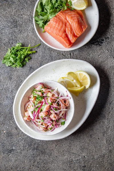 CHILEAN SALMON SEVICHE. Fresh raw salmon marinaded with purple onion, coriander in lemon juice. Ceviche and ingredientes on gray background. Top view — Stock Photo, Image