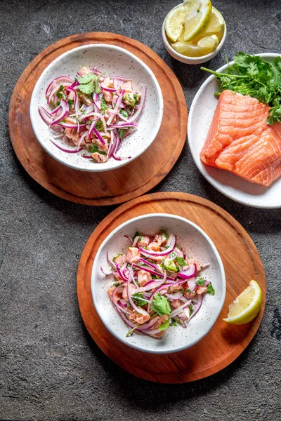 CHILEAN SALMON SEVICHE. Fresh raw salmon marinaded with purple onion, coriander in lemon juice. Ceviche and ingredientes on gray background. Top view — Stock Photo, Image