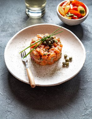 Kapari ve beyaz tabakta mor soğan ile Somon Tartar gri arka plan