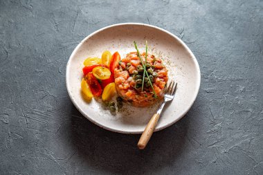 Kapari ve beyaz tabakta mor soğan ile Somon Tartar gri arka plan