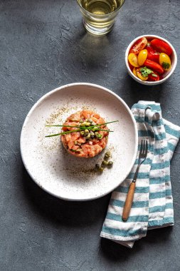 Kapari ve beyaz tabakta mor soğan ile Somon Tartar gri arka plan