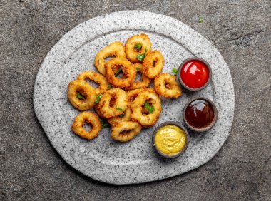 Kızarmış kalamar halkaları soslar ile gri taş plaka üzerinde. Gri beton zemin