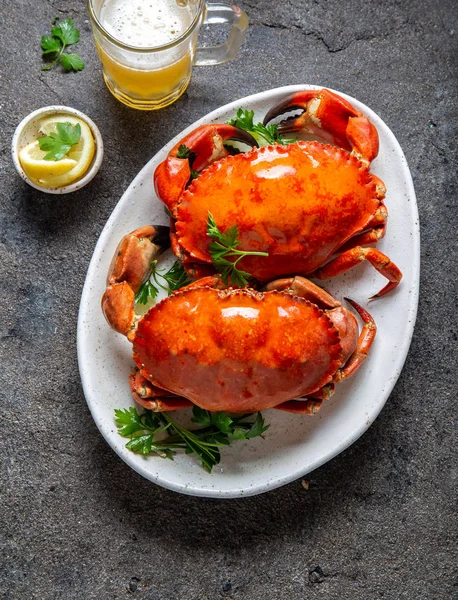 Granchi interi cotti su piatto bianco con limone e birra. Fondo in cemento grigio. Vista dall'alto — Foto Stock