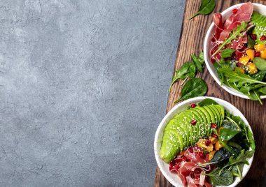 Düşük karbonhidrat kasesi. Taze salata, yeşil ıspanak, roka, avokado beyaz kasede jambon, gri arka plan, üst manzara.