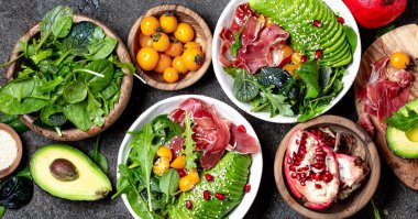 Düşük karbonhidrat kasesi. Taze salata, yeşil ıspanak, roka, avokado beyaz kasede jambon, gri arka plan, üst manzara.