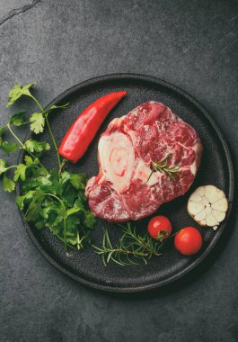 Çiğ ossobuco con şifalı otlar, sarımsak ve siyah tabakta biber. Koyu arkaplan