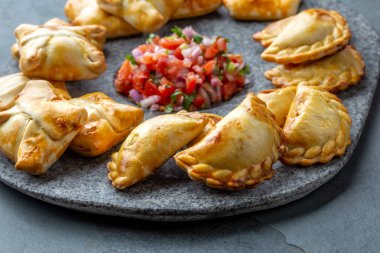 Domates sosu ve guacamole ile taş plaka üzerinde farklı küçük kokteyl Empanadas . Gri arka plan. Latin Amerika ve İspanyol tipical gıda