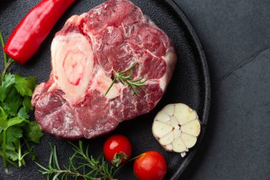 Çiğ ossobuco con şifalı otlar, sarımsak ve siyah tabakta biber. Koyu arkaplan