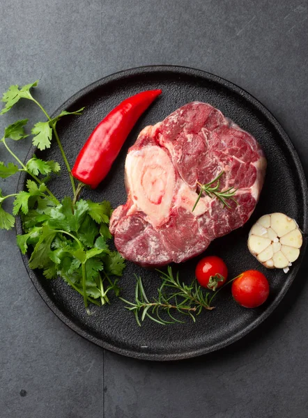 Crudo ossobuco fresco con hierbas, ajo y chile en el plato negro. Fondo oscuro — Foto de Stock