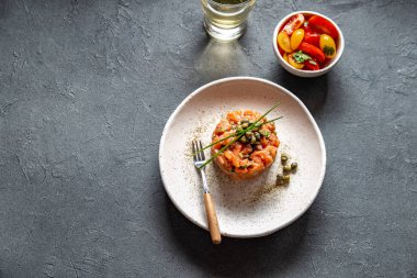 Kapari ve beyaz tabakta mor soğan ile Somon Tartar gri arka plan