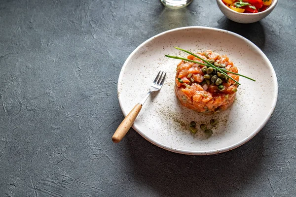 TARTAR DE SAUMON aux câpres et oignon violet sur plaque blanche, fond gris — Photo