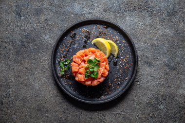 Çiğ somon, avokado mor soğan salatası ve siyah tabakta servis edilen yemek halkası. Siyah beton arkaplan