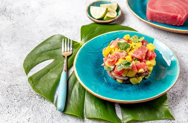 Tropisk stil gourmet tonfisk mango sallad tartar med koriander och lila lök. På blå tallrik, tropiska blad — Stockfoto