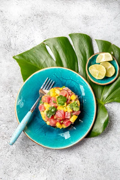 Tártaro de ensalada de mango de atún gourmet de estilo tropical con cilantro y cebolla morada. En plato azul, hojas tropicales — Foto de Stock