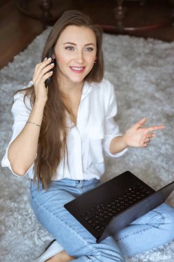 Laptop bilgisayarında çalışan ve cep telefonundan arayan beyaz bir kadın. Kadınlar evde vakit geçirir.