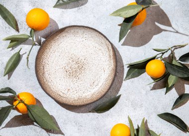 Portakal yaprakları beyaz arka planda, boş tabağın etrafında. Üst manzara, düz yatak, yaz ve sağlıklı konsept. Model