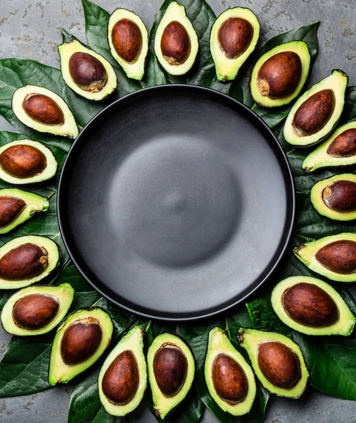 Avocado and avocado tree leaves frame around empty plate. Copy space food background.