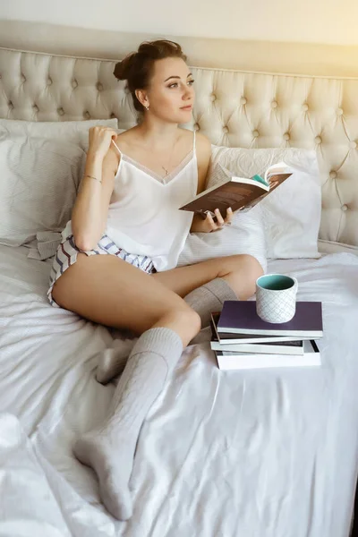 Ευτυχισμένος νέος woomen χαλαρώνοντας στο κρεβάτι και διαβάζοντας το βιβλίο μένοντας στο σπίτι. Μαθαίνοντας στο σπίτι διαβάζοντας λογοτεχνία κατά τη διάρκεια καραντίνας — Φωτογραφία Αρχείου