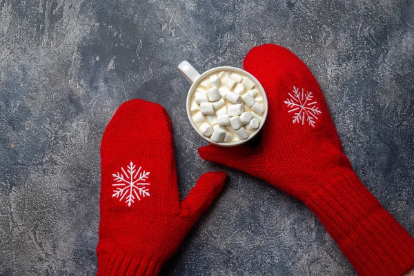Komposisi liburan Natal dan Tahun Baru yang nyaman dengan syal, tangan wanita di sarung tangan, cangkir dengan minuman panas dan marshmallow di latar belakang beton abu-abu. Letak datar, tilikan atas. — Stok Foto