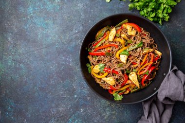 Japon karabuğdaylı soba eriştesi, tavuk ve sebzeli havuç, dolmalık biber ve lacivert arka planda yeşil fasulye.