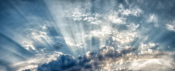 De stralen van de zon die door de wolken breken in rechte lijnen tegen de hemel en de donderwolken — Stockfoto