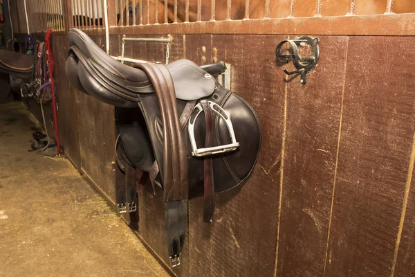 Competitive saddle of dark brown leather hanging on the bracket with leather cinch with rhinestones — Stock Photo, Image