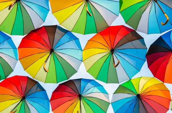 a collection of open umbrellas floating in the air, each umbrella is painted in all colors of the rainbow, photographed from below