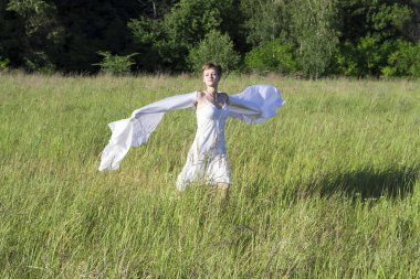 Kısa saçlı, beyaz elbiseli neşeli bir kız, elinde beyaz bir bezle tarlada koşuyor.