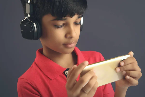 インドの若いです男の子リッスン音楽とともにヘッドフォンと保持携帯電話 — ストック写真