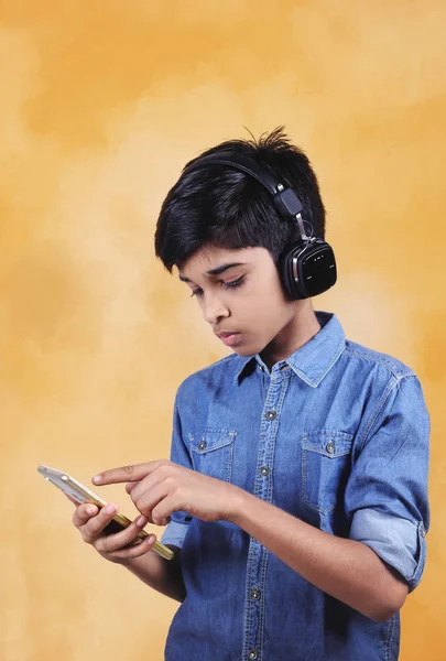 インドの若いです男の子リッスン音楽とともにヘッドフォンと保持携帯電話 — ストック写真