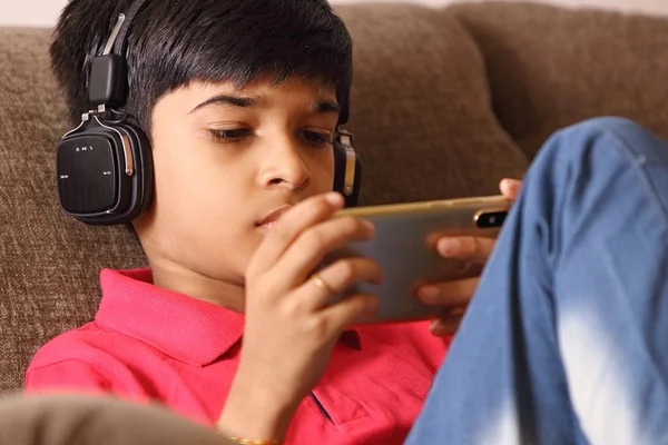 インドの若いです男の子リッスン音楽とともにヘッドフォンと保持携帯電話 — ストック写真