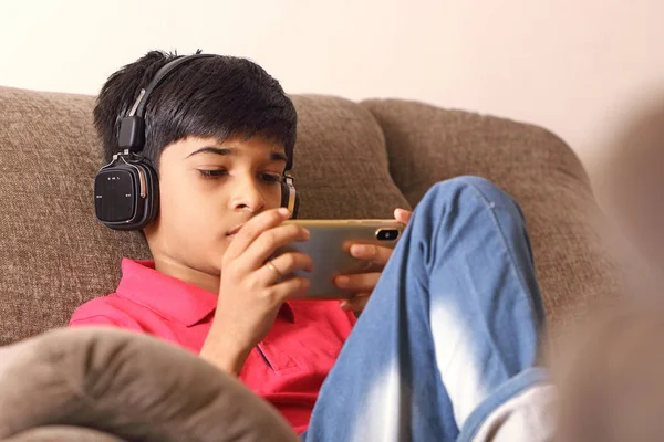 インドの若いです男の子リッスン音楽とともにヘッドフォンと保持携帯電話 — ストック写真