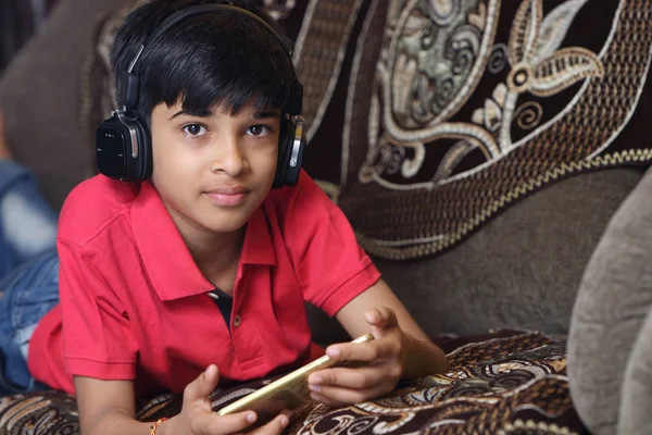 インドの若いです男の子リッスン音楽とともにヘッドフォンと保持携帯電話 — ストック写真