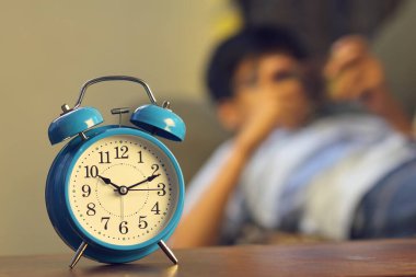 Hintli çocuk akıllı telefondan video oyunu oynuyor. Alarmlı saat onun önünde.