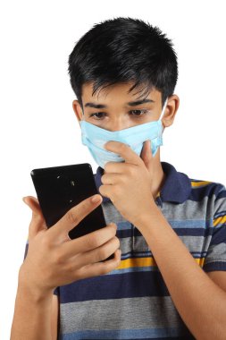 Cep telefonu kullanan ve Coronavirus Covid19 'a karşı maske takan Hintli genç bir çocuğun portresi.