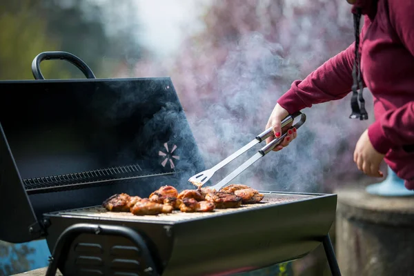 Jovem mulher grelha algum tipo de carne marinada e vegetal na churrasqueira a gás durante o verão, churrasco — Fotografia de Stock